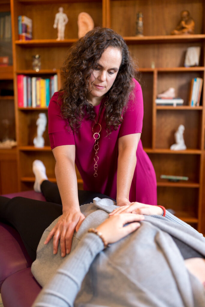 Dark haired woman massaging a client's belly as they lay on a table